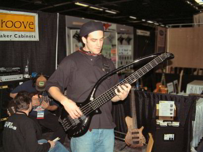 Jake Wolf at NAMM, playing the black BassLab L-BOW-V. Behind him is Skip of Knuckle Guitar Works and Jean Baudin playing his 9-string Pacman Conklin.